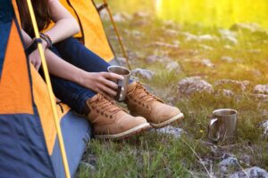 Young woman wearing lace up boots holding a coffee cup out of a yellow tent. Mornings like this are why to seek out the best camping near dallas tx!