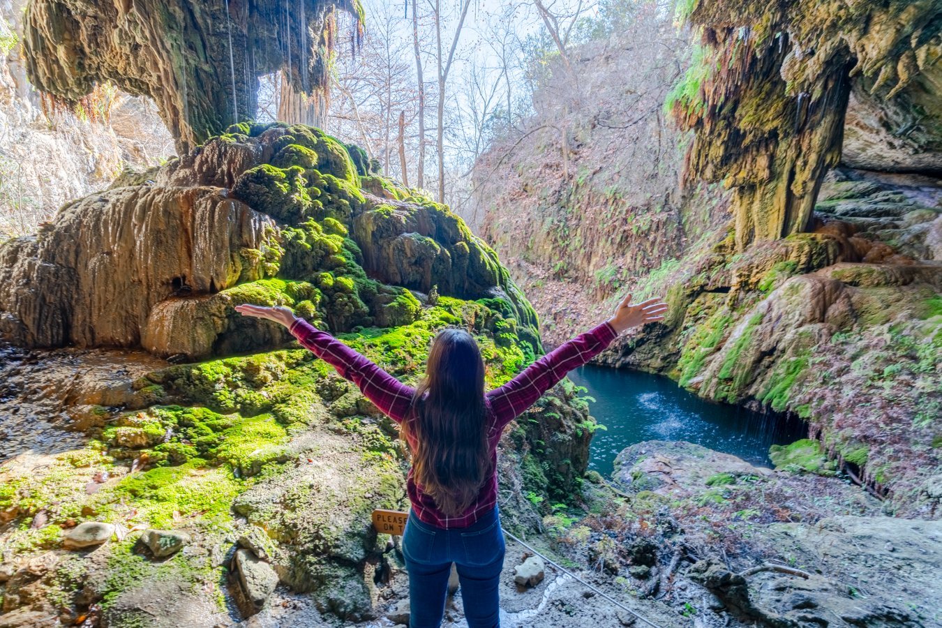 kate storm standing with her arms spread in front of westcave preserve texas waterfall