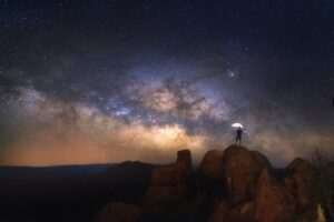 man standing on a boulder in west texas, enjoying some of the best stargazing in texas with milky way in background