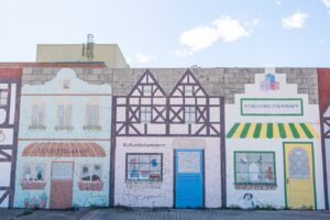 mural displaying painted german-style buildings, one of the best things to do in muenster texas is snap photos here