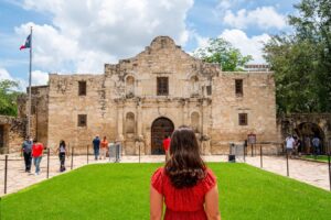 kate storm in a red dress standing facing the alamo when visiting the alamo in san antonio tx
