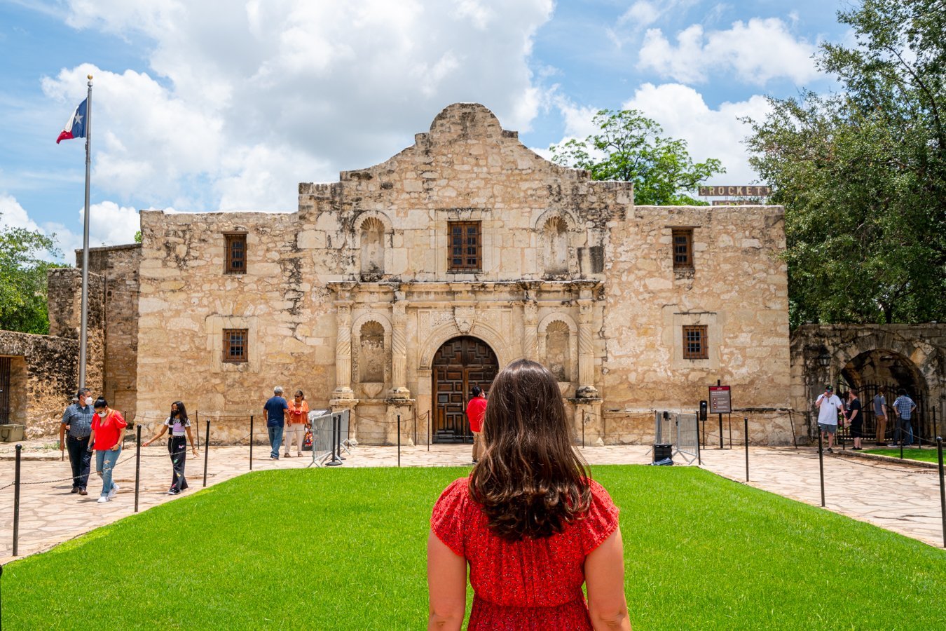 kate storm in a red dress standing facing the alamo when visiting the alamo in san antonio tx