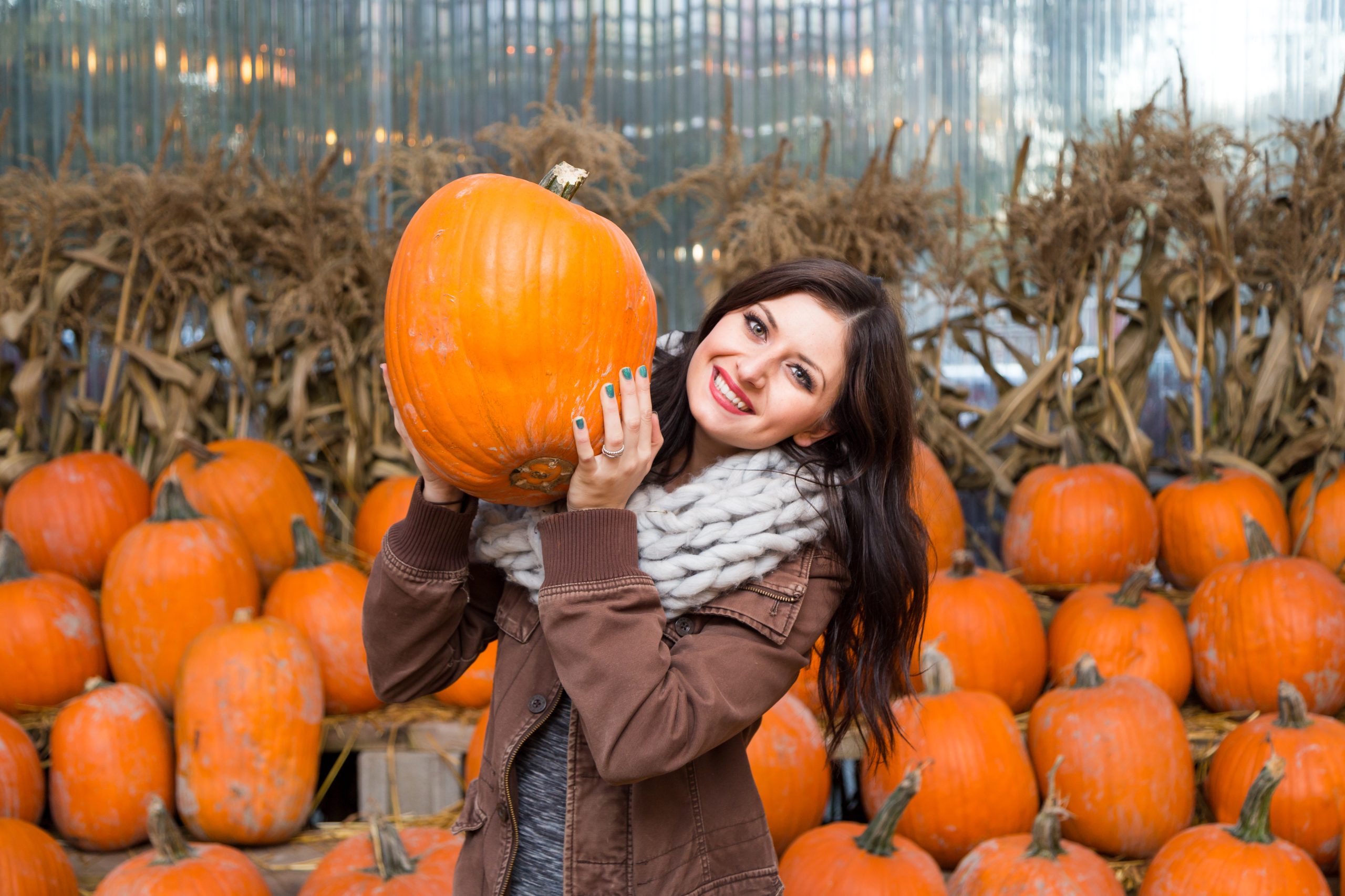 young woman with brown hair holding up a pumpkin at one of the best pumpkin patches in houston texas
